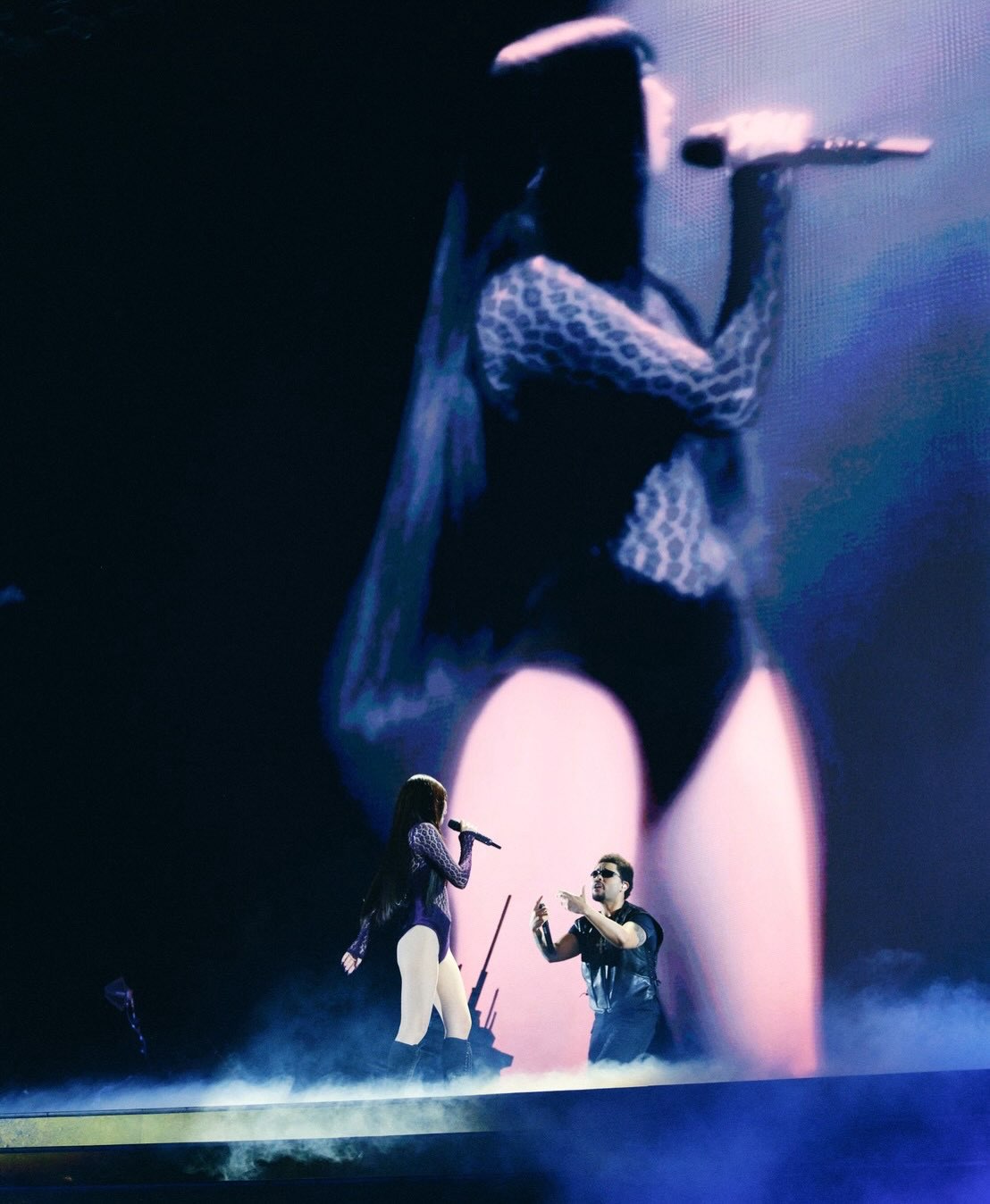 JENNIE and The Weeknd performing under blue light in front of a giant screen